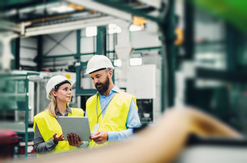 Zwei Mitarbeiter:A portrait of an industrial man and woman engineer with tablet in a factory.innen in der Fabrik